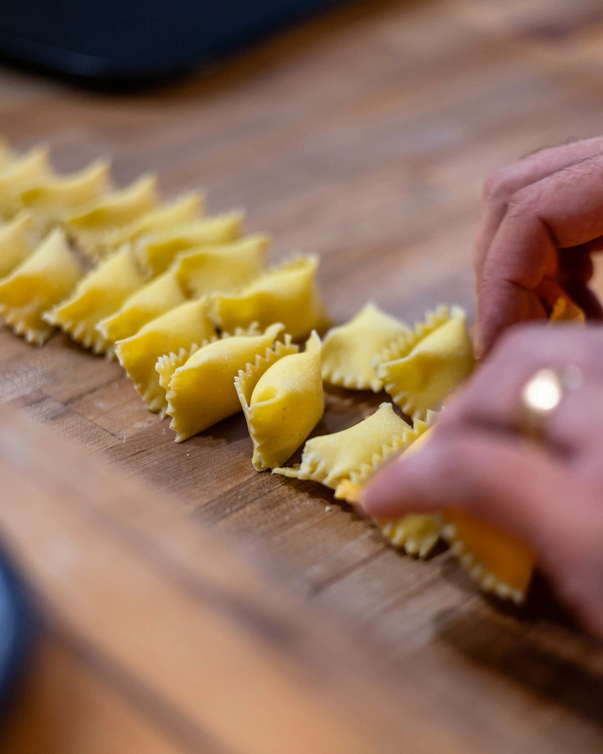 Chef shaping fresh agnolotti pasta on wooden board